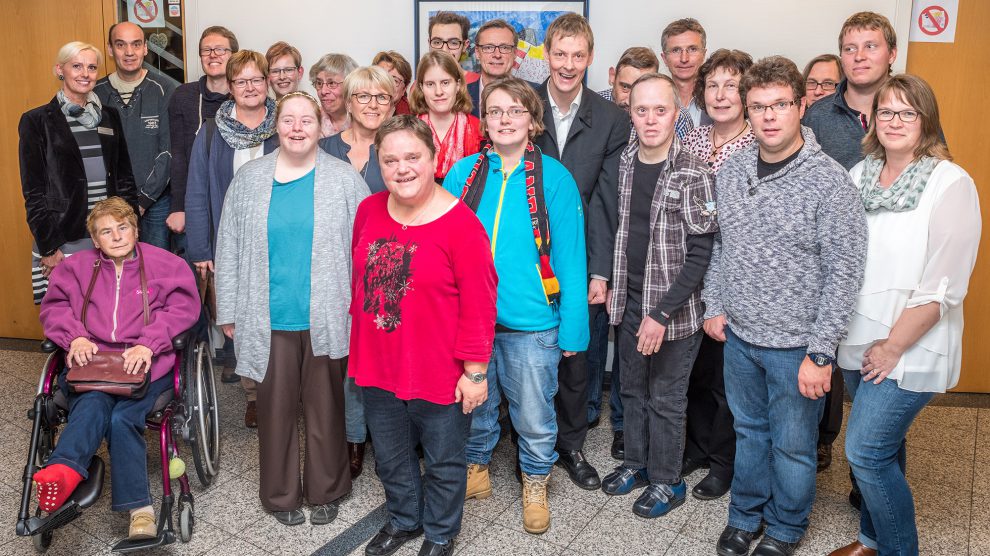 Stolz präsentiert die Künstlergruppe ihre insgesamt 20 Werke im Foyer des Wallenhorster Rathauses, hier mit Margret Terglane (links) von der Gemeindeverwaltung, Bürgermeister Otto Steinkamp (Mitte) und HHO-Geschäftsführer Heiner Böckmann (6. von rechts). Foto: Gemeinde Wallenhorst / Thomas Remme