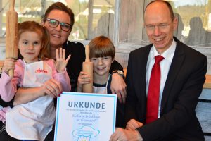 In der Bäckerei Brinkhege können sich Kinder auch als Nachwuchsbäcker versuchen, so wie hier Alyssa Lucia (5) und Fynn-Luca (7). Landrat Michael Lübbersmann überreichte Geschäftsführerin Heike Brinkhege das Zertifikat "Familienfreundliche Gastronomie". Foto: Landkreis Osnabrück/Henning Müller-Detert