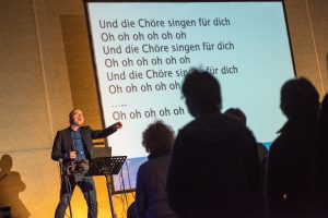 Die Chöre singen nicht nur für ihn, sondern vor allem für sich selbst – David Rauterberg unterstützt auf der Bühne mit Musik und Text. Foto: Thomas Remme