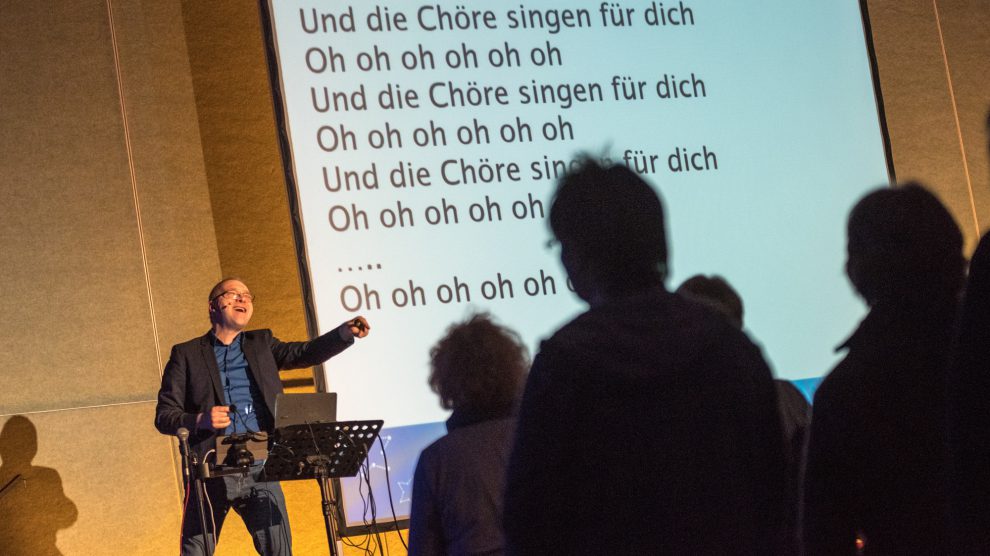 Die Chöre singen nicht nur für ihn, sondern vor allem für sich selbst – David Rauterberg unterstützt auf der Bühne mit Musik und Text. Foto: Thomas Remme