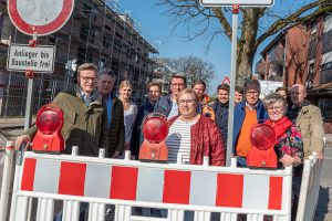 Ortstermin zum Baubeginn mit Bürgermeister Otto Steinkamp (links), Vertretern von Rat und Verwaltung, Planungsbüro, Sanierungsträger und Bauunternehmen. Links im Hintergrund der wachsende Gebäudekomplex „Wallenhorst 21“. Foto: Thomas Remme / Gemeinde Wallenhorst