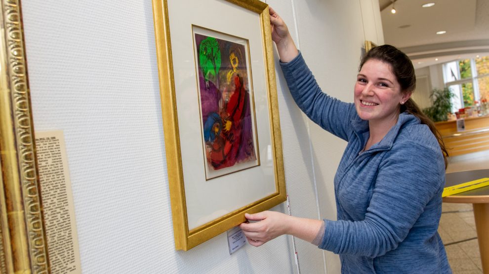 Nina Ollmert (Kunsthandlung Hülsmeier) hängt die Lithographien im Foyer des Wallenhorster Rathauses auf. Foto: Gemeinde Wallenhorst / André Thöle