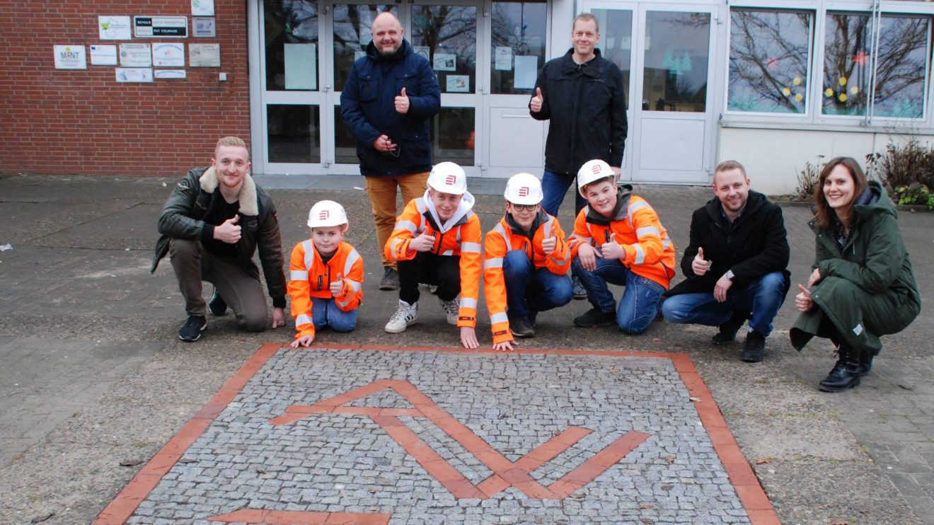 Vier Schüler der Alexanderschule in Wallenhorst haben in einer GenerationenWerkstatt mit dem Unternehmen Eiffage Infra-Nordwest eine Bodenplatte aus Natursteinen mit dem Motiv des Schullogos aus Klinkersteinen gebaut. Foto: Babette Rüscher-Ufermann / Ursachenstiftung Osnabrück