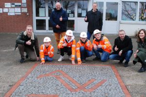 Vier Schüler der Alexanderschule in Wallenhorst haben in einer GenerationenWerkstatt mit dem Unternehmen Eiffage Infra-Nordwest eine Bodenplatte aus Natursteinen mit dem Motiv des Schullogos aus Klinkersteinen gebaut. Foto: Babette Rüscher-Ufermann / Ursachenstiftung Osnabrück