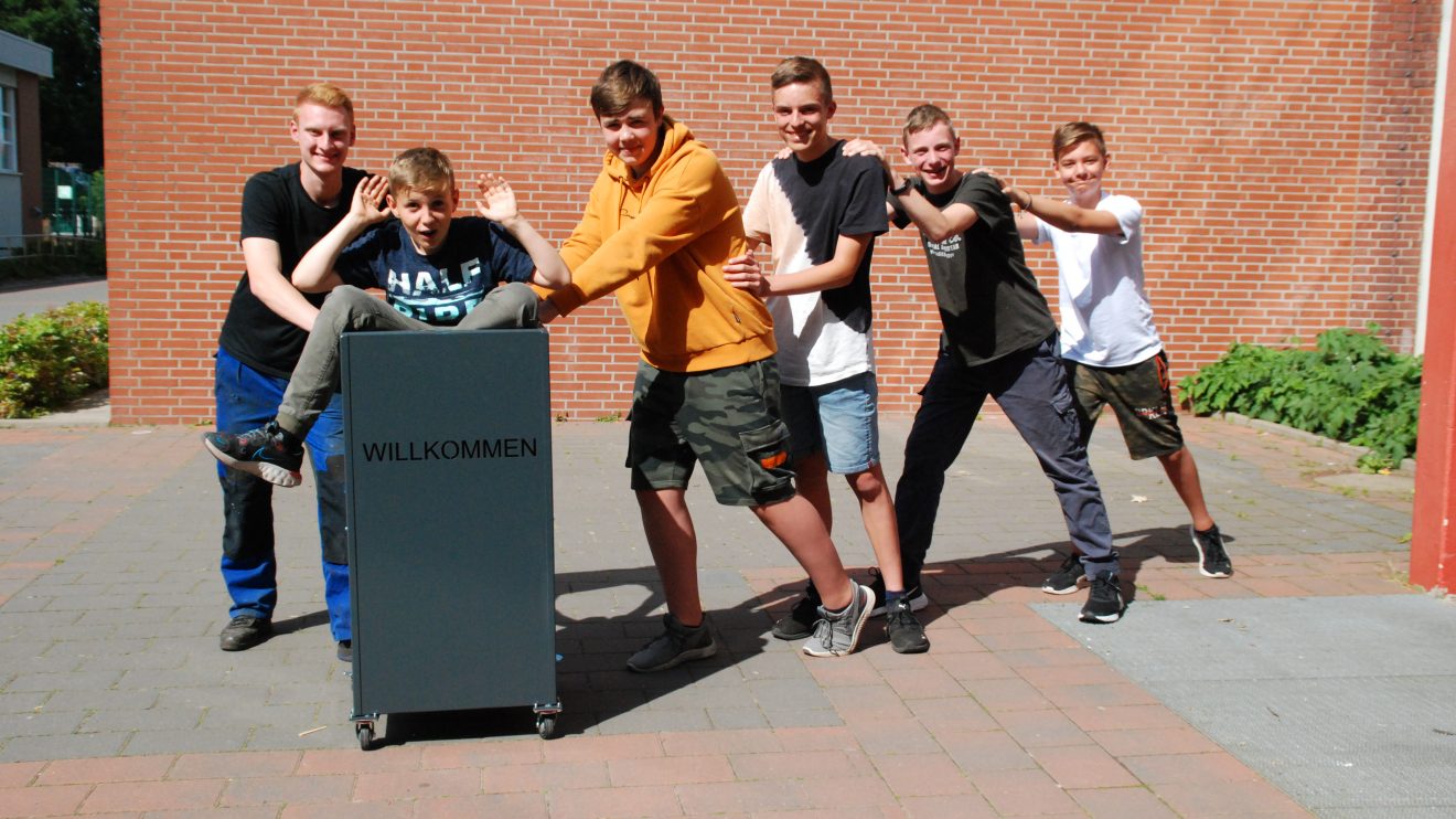 Alles ist möglich mit diesem multifunktionalen, rollbaren Moderationswagen. Auch Mitschüler können damit transportiert werden. Marlon (Auszubildender Purplan) und Max (im Wagen), Oliver, Henri, Jonas und Louis, Schüler der Realschule Wallenhorst, freuen sich über ihr vielfältig einsetzbares Projektergebnis. Foto: Babette Rüscher-Ufermann