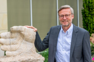 Bürgermeister Otto Steinkamp neben der vor dem Rathaus stehenden Skulptur „Stein des Anstoßes“, an der die Namen der bisherigen Preisträgerinnen und Preisträger zu sehen sind. Foto: André Thöle