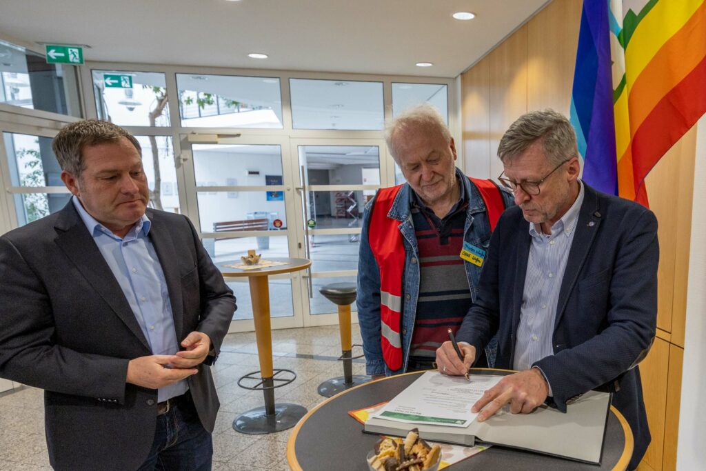 Bürgermeister Otto Steinkamp unterzeichnet die Beitrittserklärung. Ratsherr Guido Pott und Johannes Bartelt von der Friedensinitiative schauen genau hin. Foto: Rüdiger Mittmann