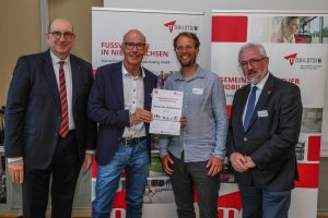 Matthias Wunderling-Weilbier überreicht die Urkunde für den „Fußverkehrs-Check“ an Rüdiger Mittmann und Stefan Brune im Beisein von Christian Berndt (von links). Foto: LNVG/Wilde